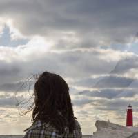Photograph featuring female-presenting figure contemplating the horizon at a beach-like setting during sunset